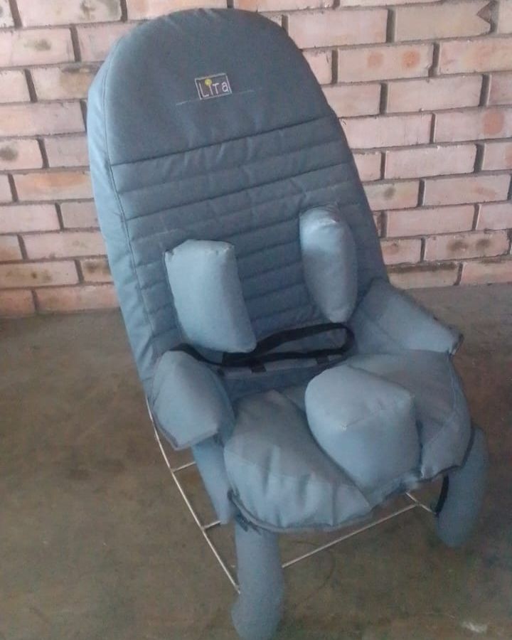 The grey LiTa Cumfy chair on its rocking frame, with padded supports for the head, body and hips and a chest strap.
