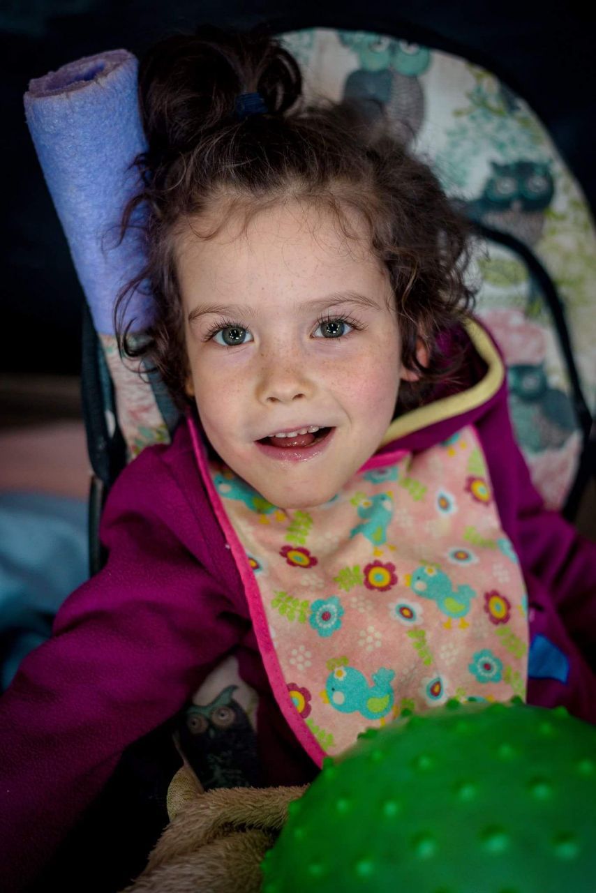 Thelita, smiling, sitting in an early prototype chair with an owl print cover, a green ball in front of her.